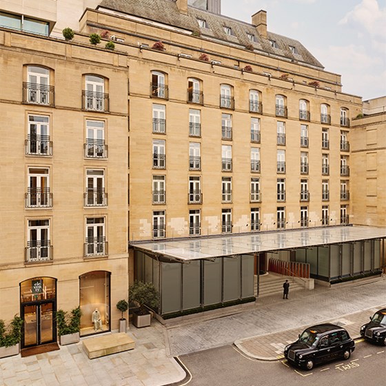 Exterior view of The Berkeley hotel in London, showcasing its elegant stone façade, modern glass canopy entrance, and black cabs parked at the kerbside.