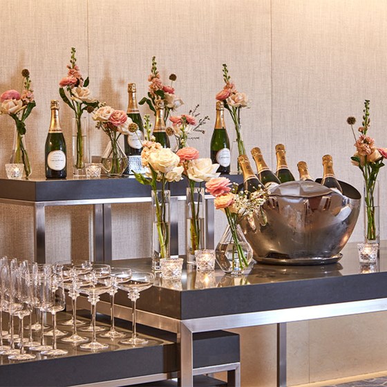 Champagne in ice buckets, champagne glasses and flower on high tables.