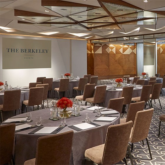 Room set up for a meeting with several round tables, papers, pens, glasses of water. At the back are two screens displaying 'The Berkeley' logo.