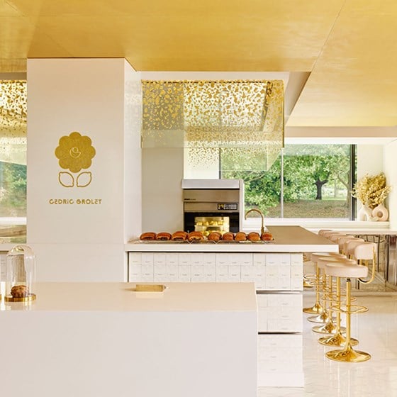 A luminous pâtisserie counter at Cedric Grolet at The Berkeley, with golden stools, pristine white surfaces, and a delicate display of viennoiserie beneath a gold-speckled canopy.