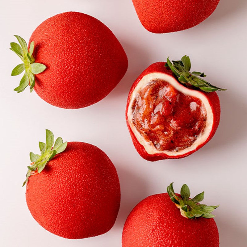 Red trompe-l’œil strawberries with a textured outer layer and green stems, one cut open to reveal a rich strawberry filling and creamy centre.