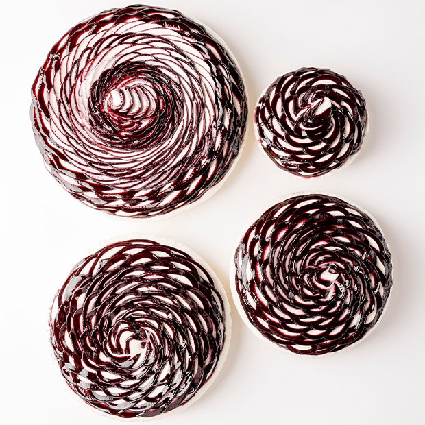 Four glossy tarts with cream spirals swirled in dark berry compote, presented on a white background in a visually balanced arrangement.