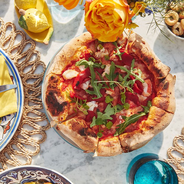 Overhead view of a freshly baked pizza topped with rocket and red peppers on a marble table.