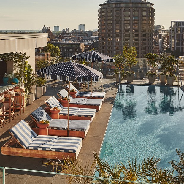 Rooftop poolside lounge at The Berkeley with striped sun loungers, parasols, and fruit bowls, overlooking a city skyline under clear skies.