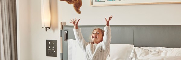 Little girl in The Berkley hotel dressing gown smiling as she throws jellycat teddy bear in the air.