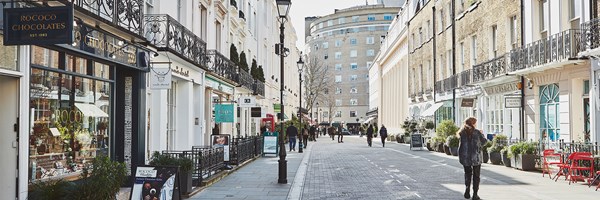 View onto Motcomb street with cobbled pavement and rows of shops.