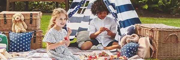 Boy and girl eating strawberries amidst picnic set up including teepee and rug on the grass