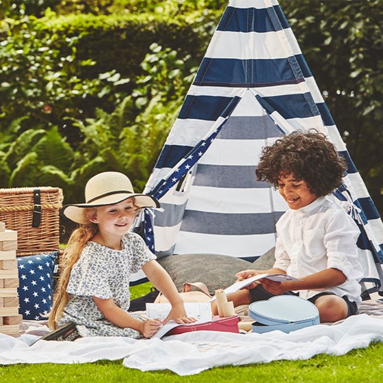 Two children playing in a garden with jenga colouring books, and a blue & white striped teepee