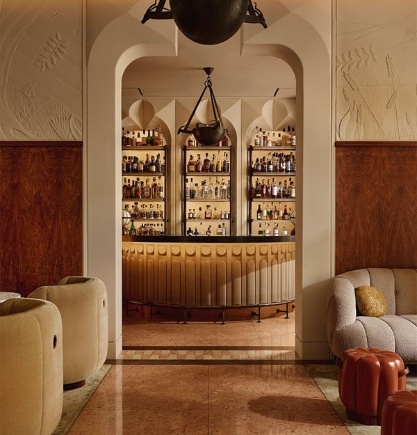 Warm, inviting bar at The Berkeley with art deco influences, featuring a sculptural archway, curved seating, and a glowing backlit display of premium spirits.