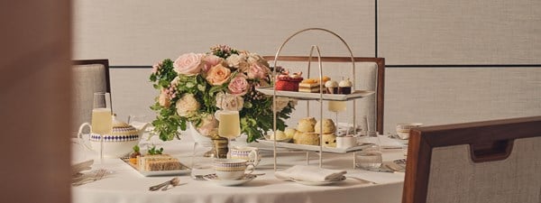 A close-up of an elegantly set round table featuring a floral centerpiece and a multi-tiered tray with afternoon tea treats, including scones and pastries.