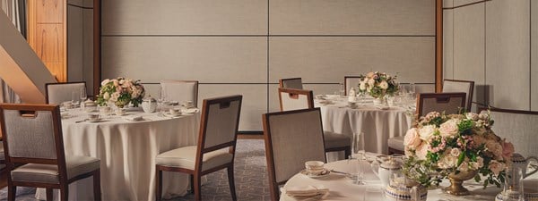 A beautifully arranged round table setup with elegant floral centerpieces in a refined event space with neutral tones and wooden accents.