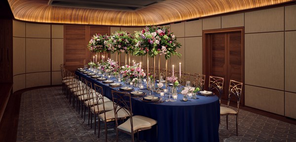 A long dinner table with a blue tablecloth set over it, with candles and bright flowers decorating the table in a small event room