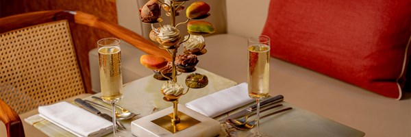 A stylish tea setting featuring an elegant golden stand displaying assorted pastries and desserts, complemented by two flutes of champagne on a marble table.