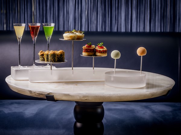 A sophisticated afternoon tea display at The Berkeley's Blue Bar, featuring a selection of artfully arranged canapés and colorful cocktails on a sleek marble table against a dark, elegant backdrop.