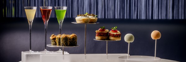 A sophisticated afternoon tea display at The Berkeley's Blue Bar, featuring a selection of artfully arranged canapés and colorful cocktails on a sleek marble table against a dark, elegant backdrop.