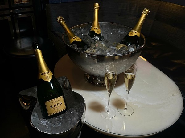 A sophisticated presentation of Krug champagne bottles in an ice-filled silver bucket, accompanied by two glasses of champagne on a marble table.