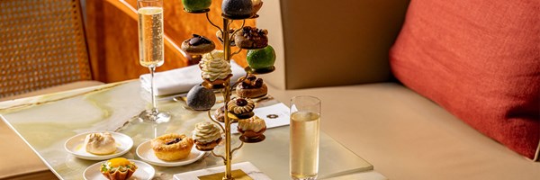 A luxurious Goutea setup featuring an elegant tower of assorted pastries and small bites, accompanied by champagne and additional plated treats on a marble table.