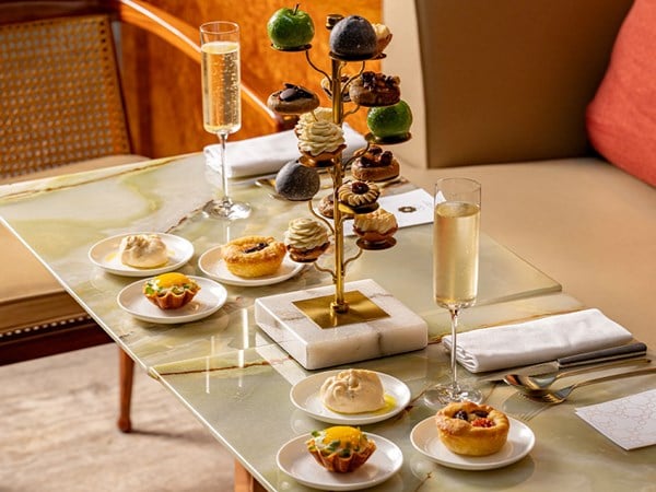 A luxurious Goutea setup featuring an elegant tower of assorted pastries and small bites, accompanied by champagne and additional plated treats on a marble table.