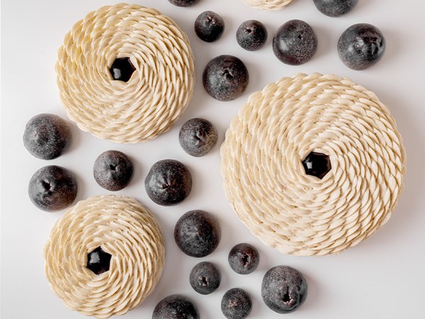 Three intricate cakes are surrounded by several mini cakes that resemble blueberries.