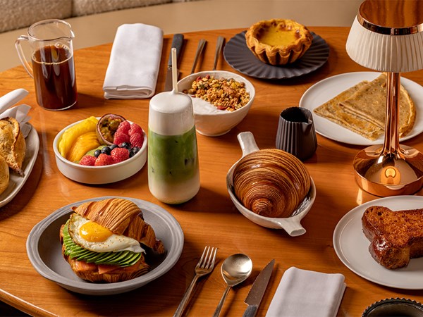 A well-arranged breakfast table with croissants, pastries, fruits, yogurt, and a green beverage.