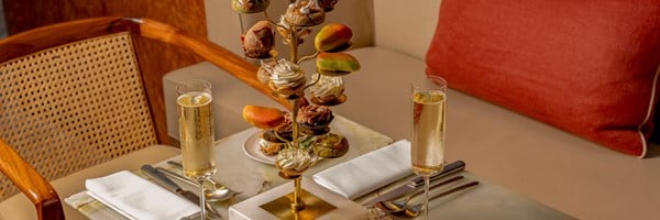 An elegant dessert presentation of Cedric Grolet's pastries displayed on a golden tree stand with glasses of champagne on a finely set table