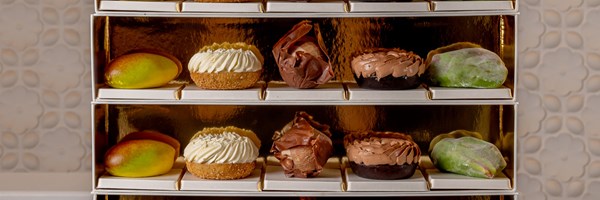 Close-up of Cedric Grolet’s pastries arranged neatly on a tiered tray, with vibrant fruit replicas and golden accents creating a luxurious aesthetic.