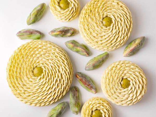 An artistic flat-lay of Cedric Grolet’s vanilla swirl pastries accompanied by pistachio-inspired creations, forming a mesmerizing pattern