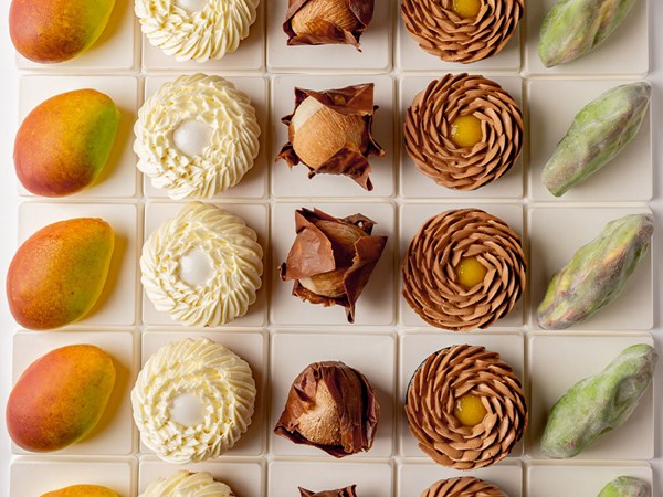 A neatly arranged grid of Cedric Grolet’s signature pastries and fruit-shaped creations, displayed in alternating rows for an artistic visual impact