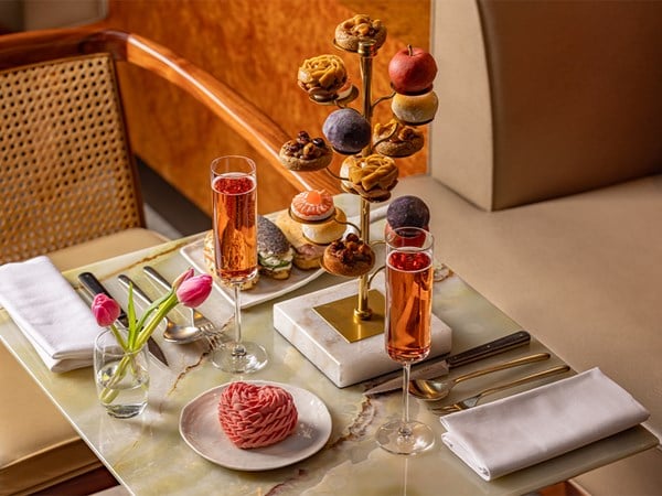 Elegant afternoon tea with pastries on a gold stand, sparkling rosé, and a pink tulip on a marble table.