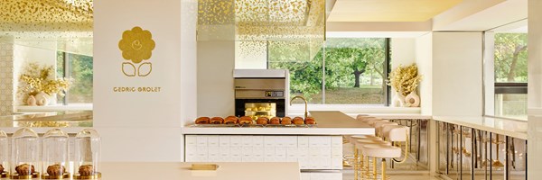 An open pastry kitchen bathed in natural light, showcasing golden accents, sleek counter seating, and a row of freshly baked creations at Cedric Grolet at The Berkeley.