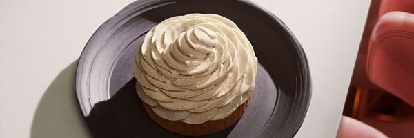 A close-up of an artful vanilla tart by Cedric Grolet, its sculptural cream swirl presented on a deep ceramic plate, radiating culinary precision and elegance.