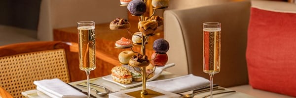 An exquisite table setting with a glass of champagne and Cedric Grolet’s signature pastry tree, adorned with intricate sweet and savoury bites for afternoon tea.