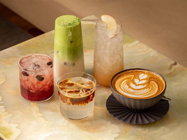 A selection of five colourful drinks on a marble table, including matcha latte, iced espresso, fruit soda, and latte with latte art.