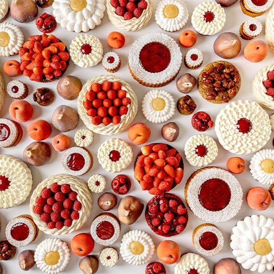 A neat row of daisy-like tartlets topped with white piped cream and vibrant yellow centres, resembling summer flowers on a white background.