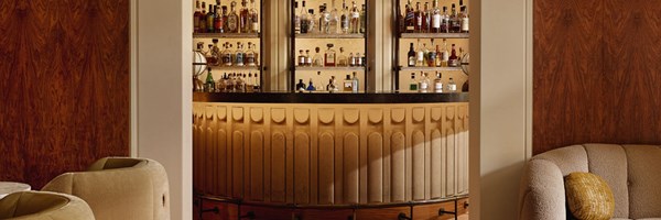 A sophisticated view of The Berkeley Bar’s sculpted central counter framed by warm wood panelling, with an elegant backlit display of rare spirits and liquors.