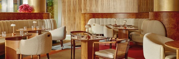 The Berkeley Café’s intimate seating area, showcasing warm wooden paneling, plush cream banquettes, and delicate table lamps accenting each table.