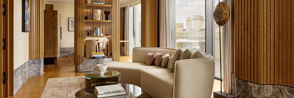 A bright and contemporary living space with curved cream seating, fluted wood wall accents, glass doors opening to a terrace, and a bespoke shelving divider framing the dining area.