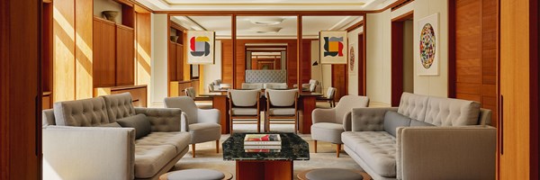 An elegant open-plan living and dining space with mid-century modern grey armchairs, warm wood paneling, and abstract art adorning the walls.