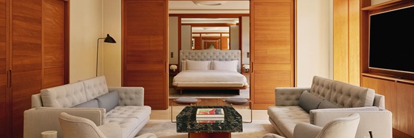 A sophisticated suite interior with a view from the lounge area toward the bedroom, featuring matching tufted seating and a central coffee table in dark stone.