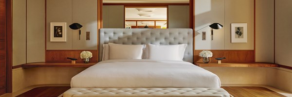 A tranquil bedroom with a plush, button-tufted headboard, crisp white linens, and built-in wood shelving beneath softly lit wall panels.