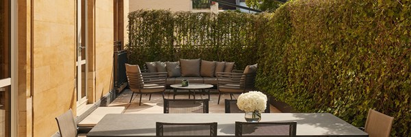 A secluded outdoor terrace framed by ivy-covered walls, featuring a dining table and a cosy corner sofa set for alfresco relaxation.