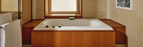 A serene bathroom featuring a sunken white bathtub framed in warm wood, positioned beneath a frosted window for natural light and privacy.