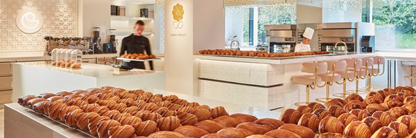 A modern bakery with elegant decor showcases rows of freshly baked croissants, as chefs and staff prepare pastries in a sleek, open kitchen.