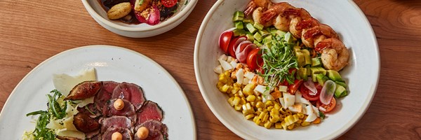 A selection of refined dishes including a shrimp salad, tender carpaccio, and roasted vegetables, presented with rustic charm.